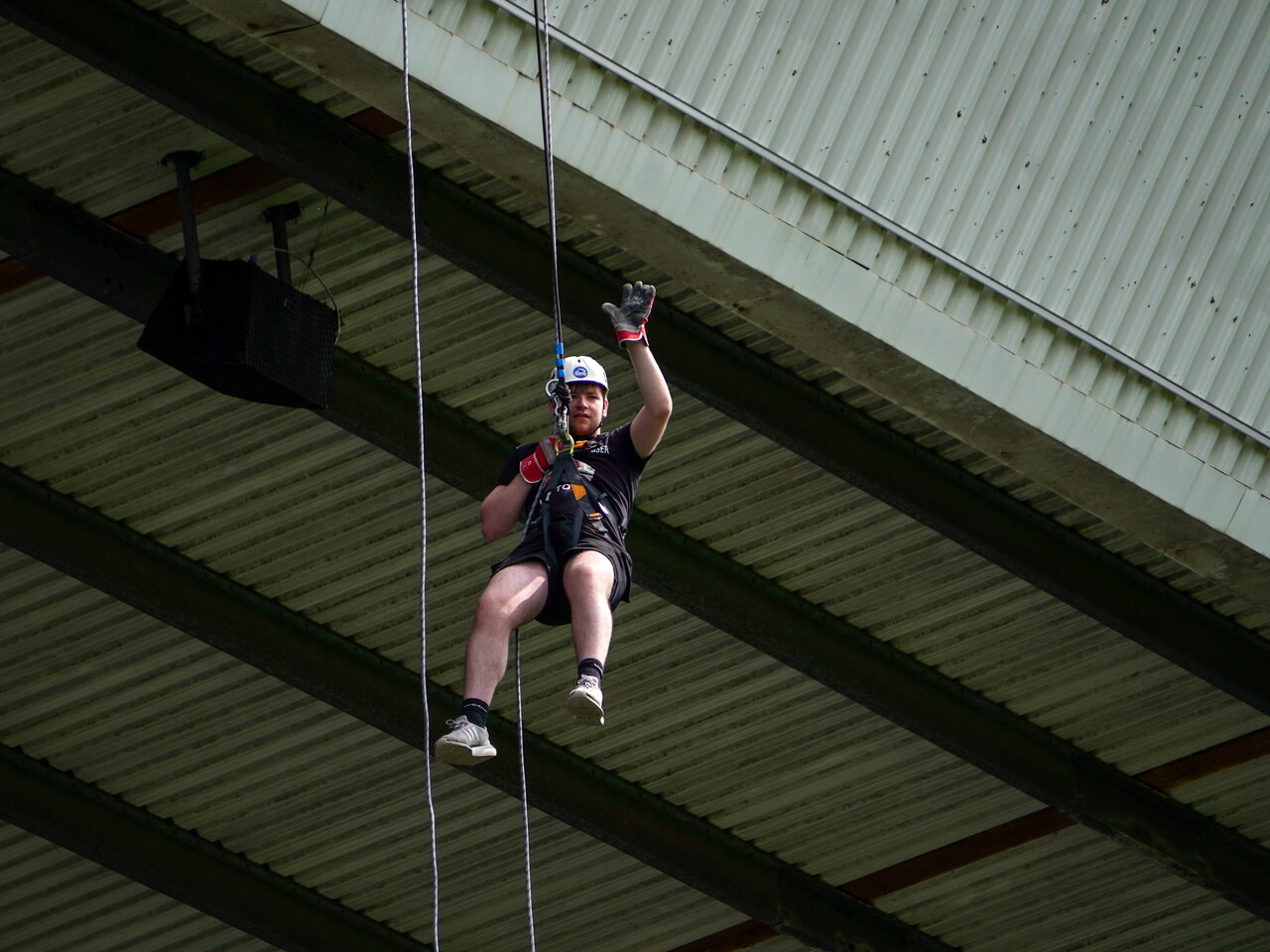 Participant wearing a helmet and harness waves while abseiling beneath the stadium roof at The Hawthorns.