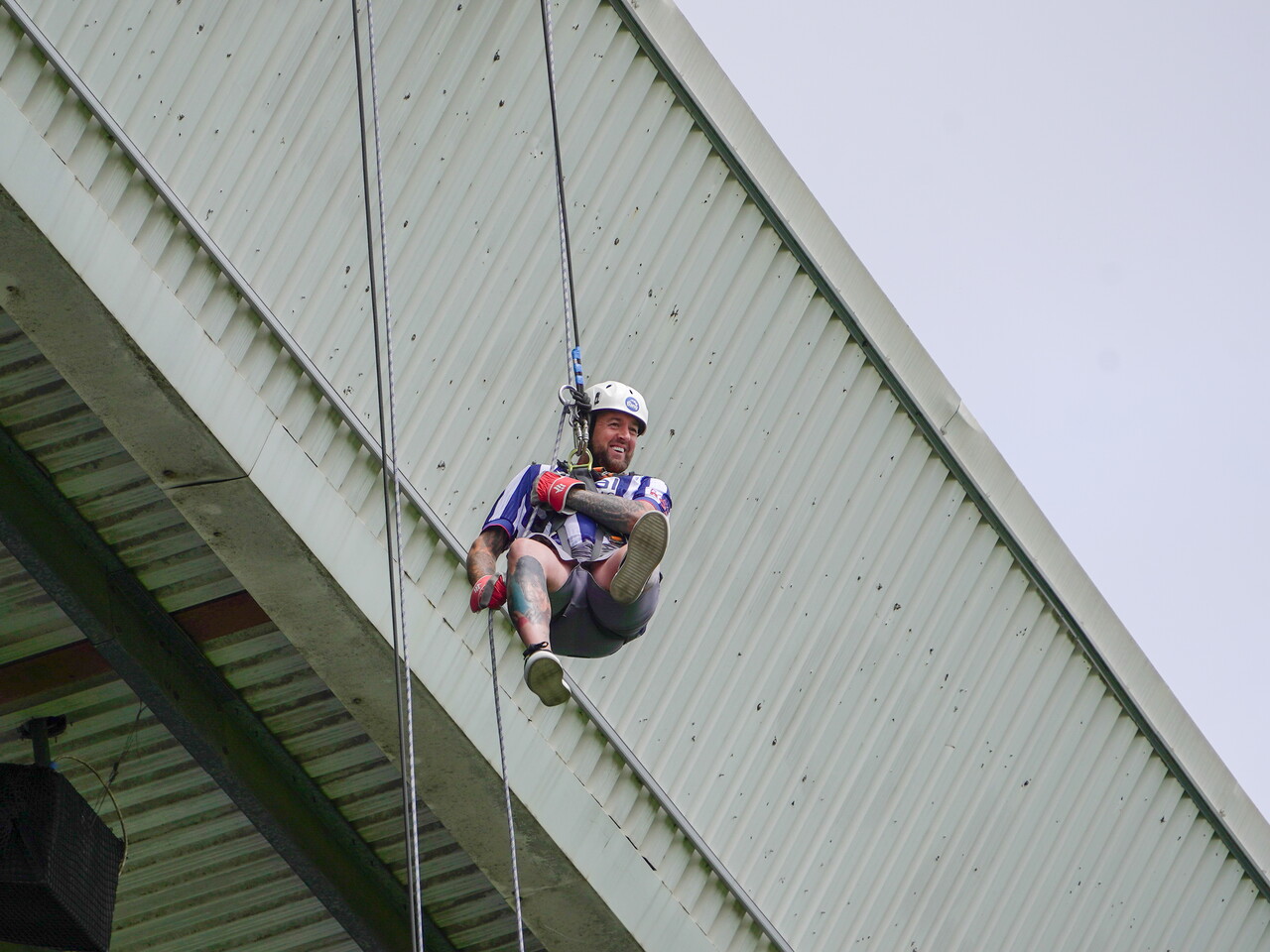 Participant wearing a helmet, harness and safety gloves abseils from the roof of The Hawthorns during a charity abseil event.