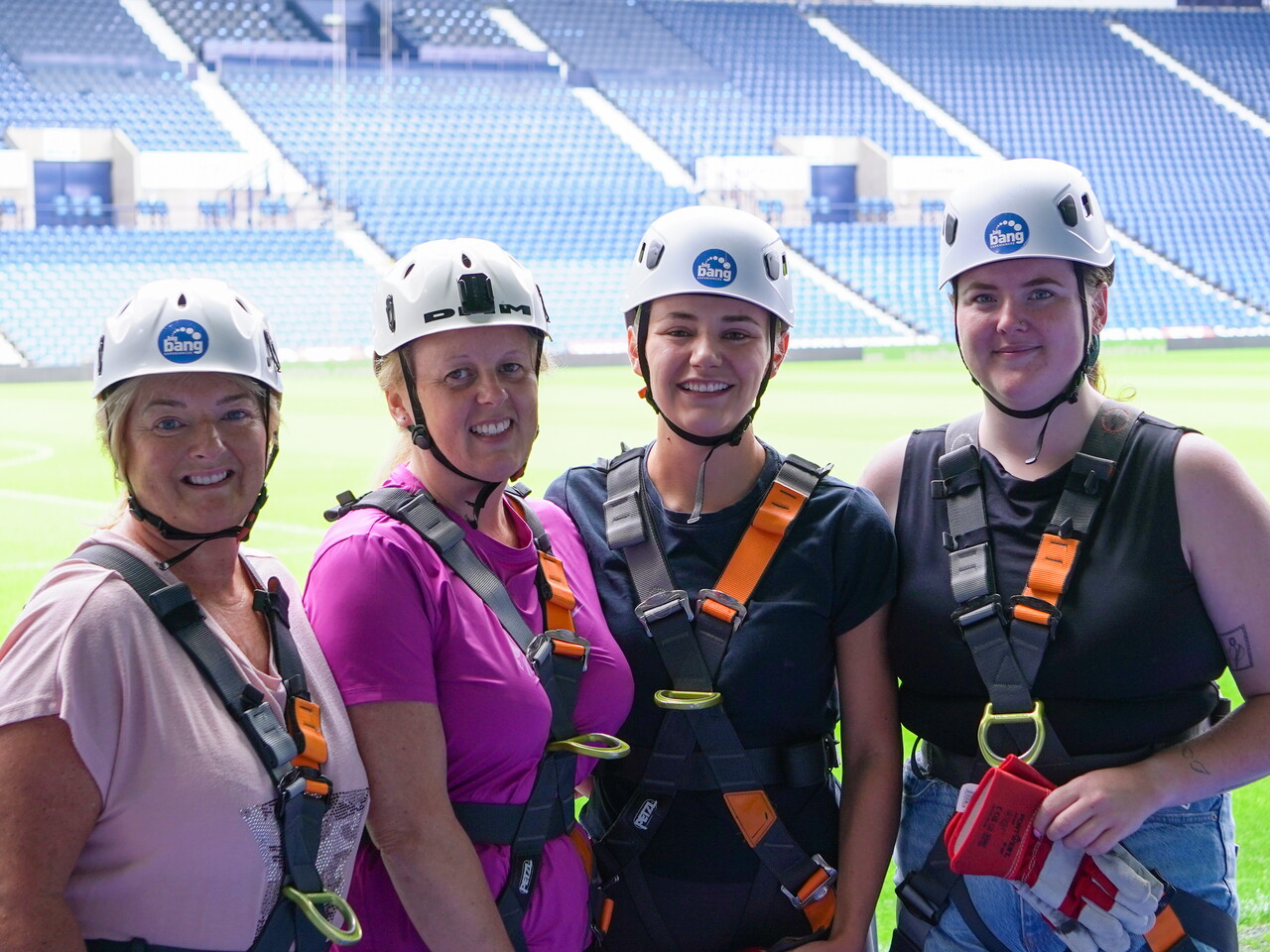 Four participants wearing helmets and safety harnesses pose for a photo at The Hawthorns, with the pitch and stadium seating visible behind them.