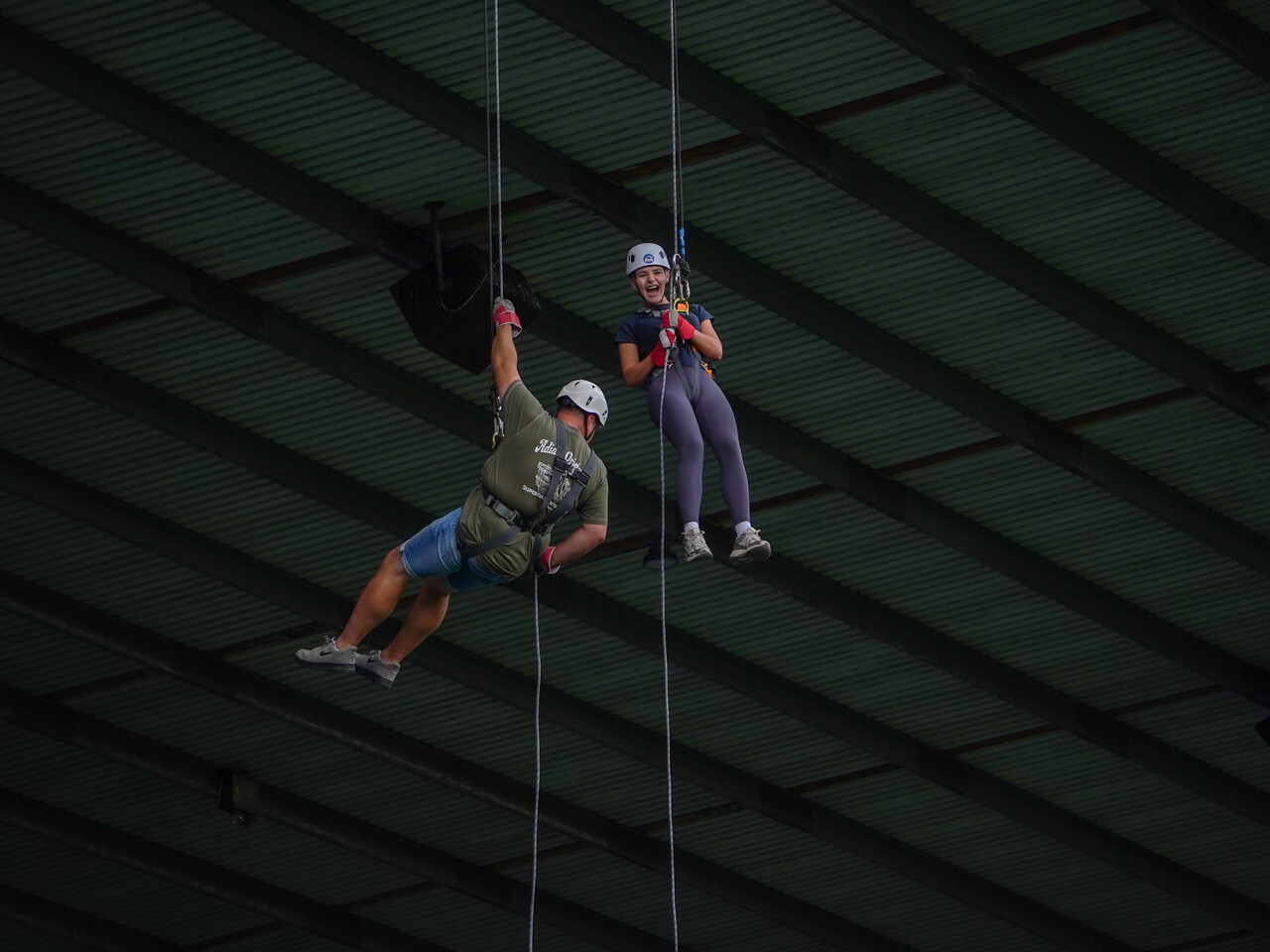 Two participants wearing helmets and harnesses abseil side by side beneath the stadium roof during a charity abseil event at The Hawthorns.