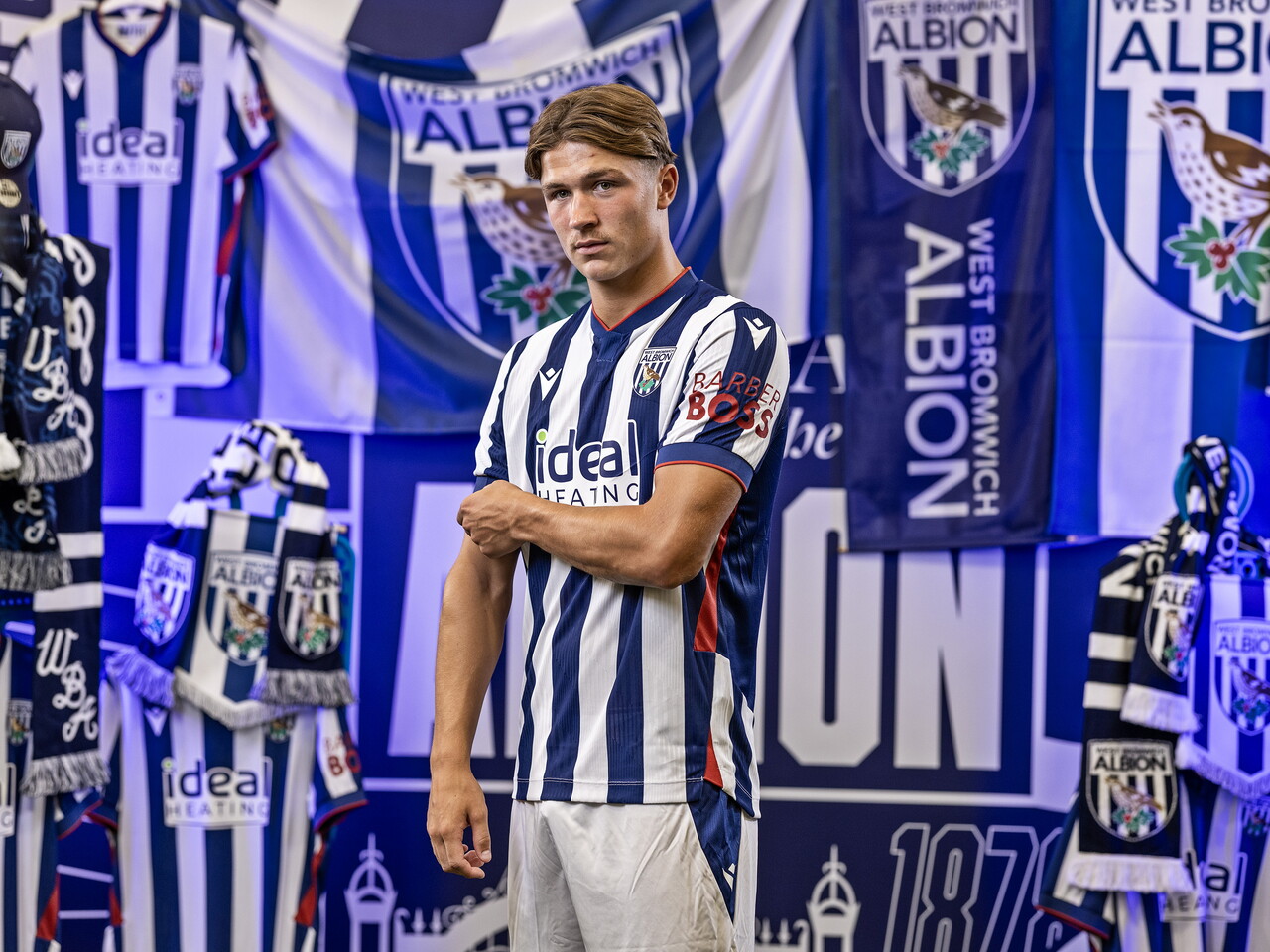 Cole Deeming in the home kit looking at the camera while stood in front of an Albion back drop with plenty of WBA branding