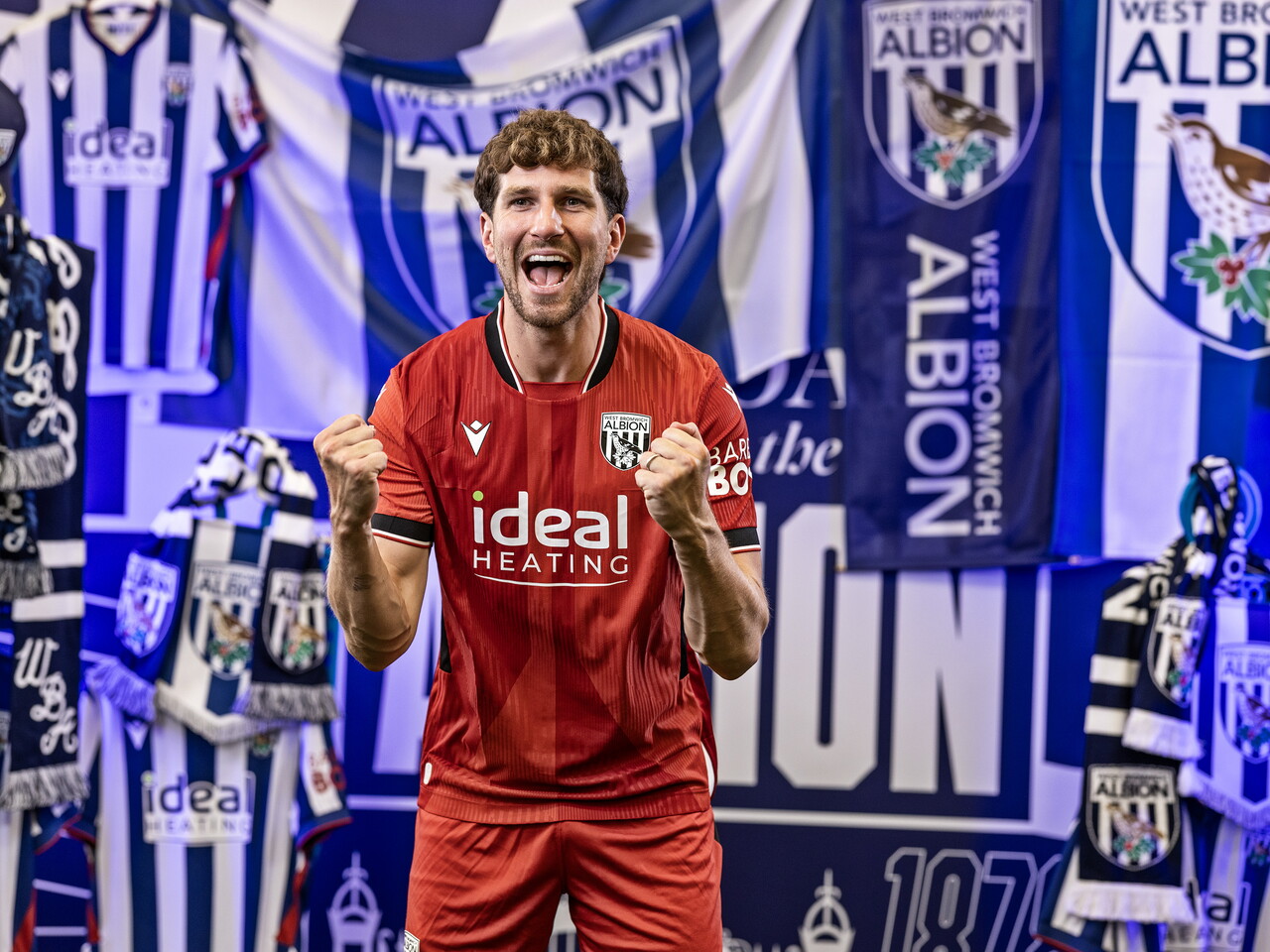 Chris Mepham in the red away kit celebrating towards the camera while stood in front of an Albion back drop with plenty of WBA branding