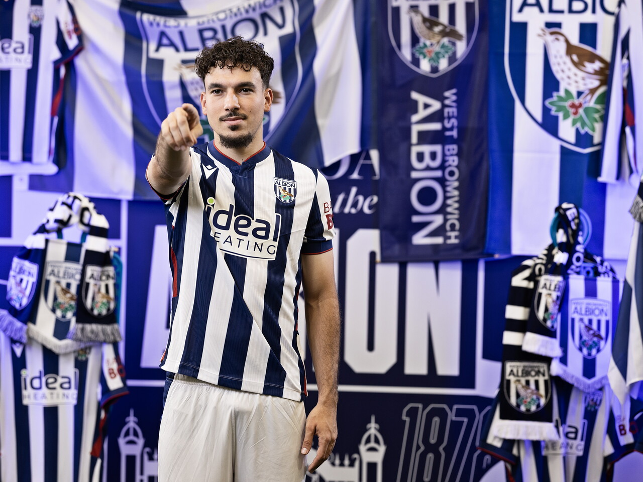 Nolan Galves in the home kit pointing at the camera while stood in front of an Albion back drop with plenty of WBA branding