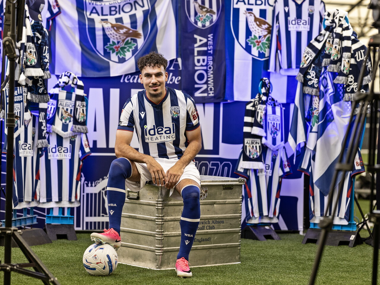 Nolan Galves in the home kit with his foot on a ball while sat on a kit skip in front of an Albion back drop with plenty of WBA branding