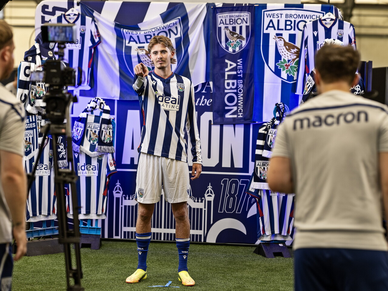 Isaac Price in the home kit pointing at the camera while stood in front of an Albion back drop with plenty of WBA branding