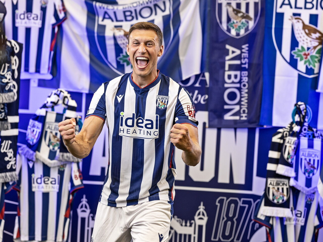 Krystian Bielik celebrating towards the camera while stood in the home shirt in front of an Albion back drop with plenty of WBA branding