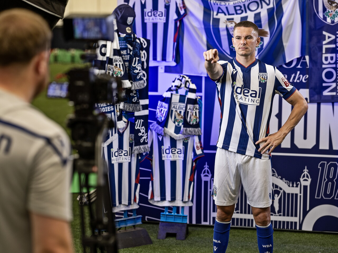 Conor Townsend in the home kit pointing at the camera while stood in front of an Albion back drop with plenty of WBA branding