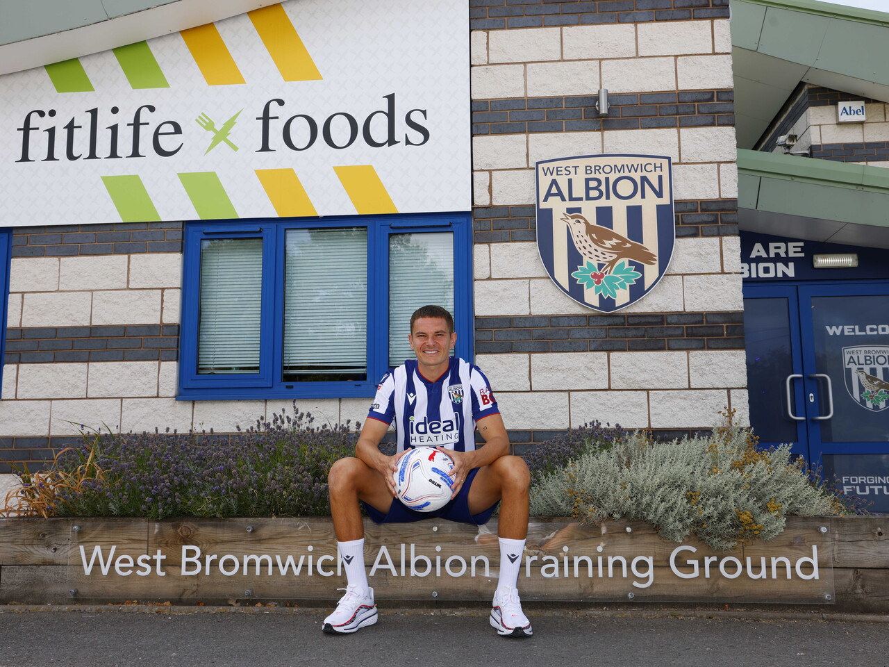 Conor Townsend sat outside the WBA training ground in the home shirt holding a ball