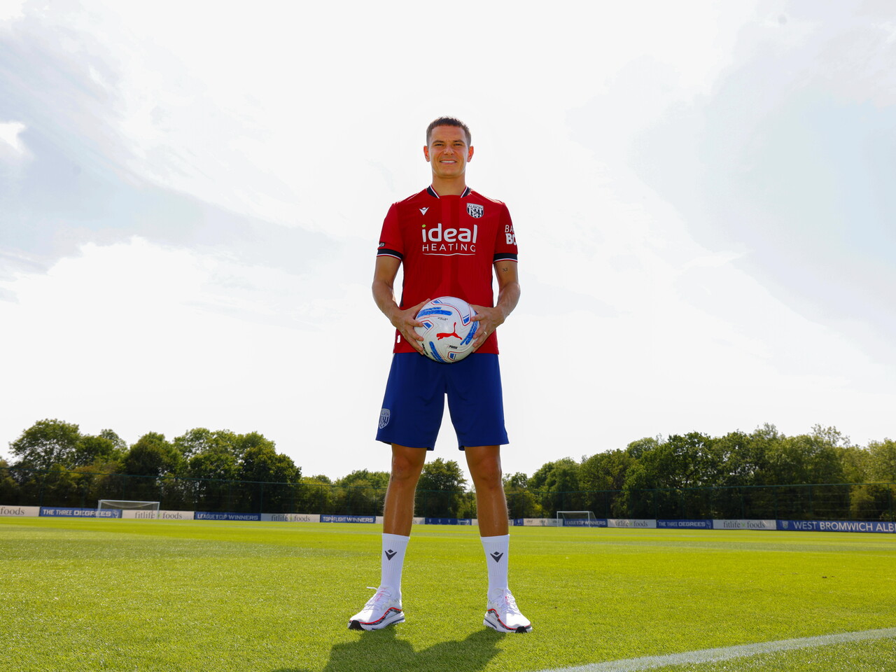 Conor Townsend smiling at the camera while stood in the away kit out on a training pitch and holding a ball
