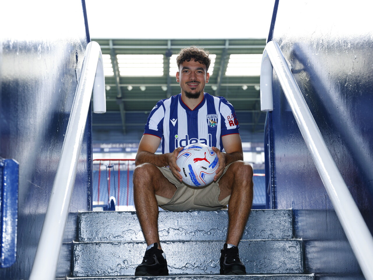 Nolan Galves sat on a step at The Hawthorns in the home kit holding a ball