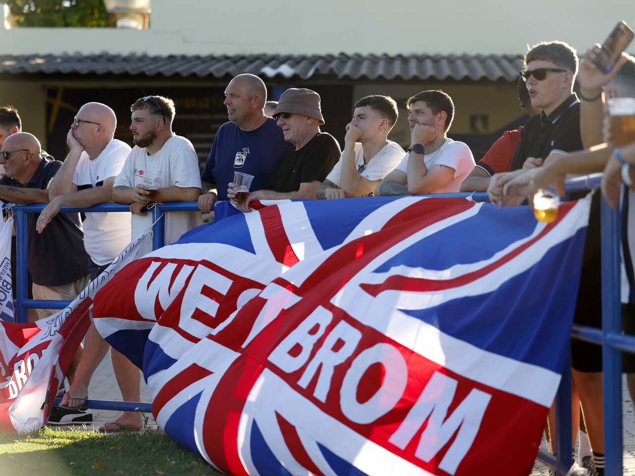 Several WBA fans pose for a photo in front of a WBA flag 