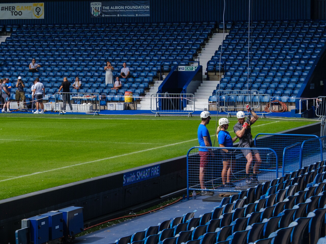 Participant completes an abseil at pitchside at The Hawthorns, with support staff, spectators and rows of blue seats visible in the background.Provide your feedback on BizChatAdd alt text for the next imageDescribe the abseiling setupWhat safety checks are visible?FilesFiles