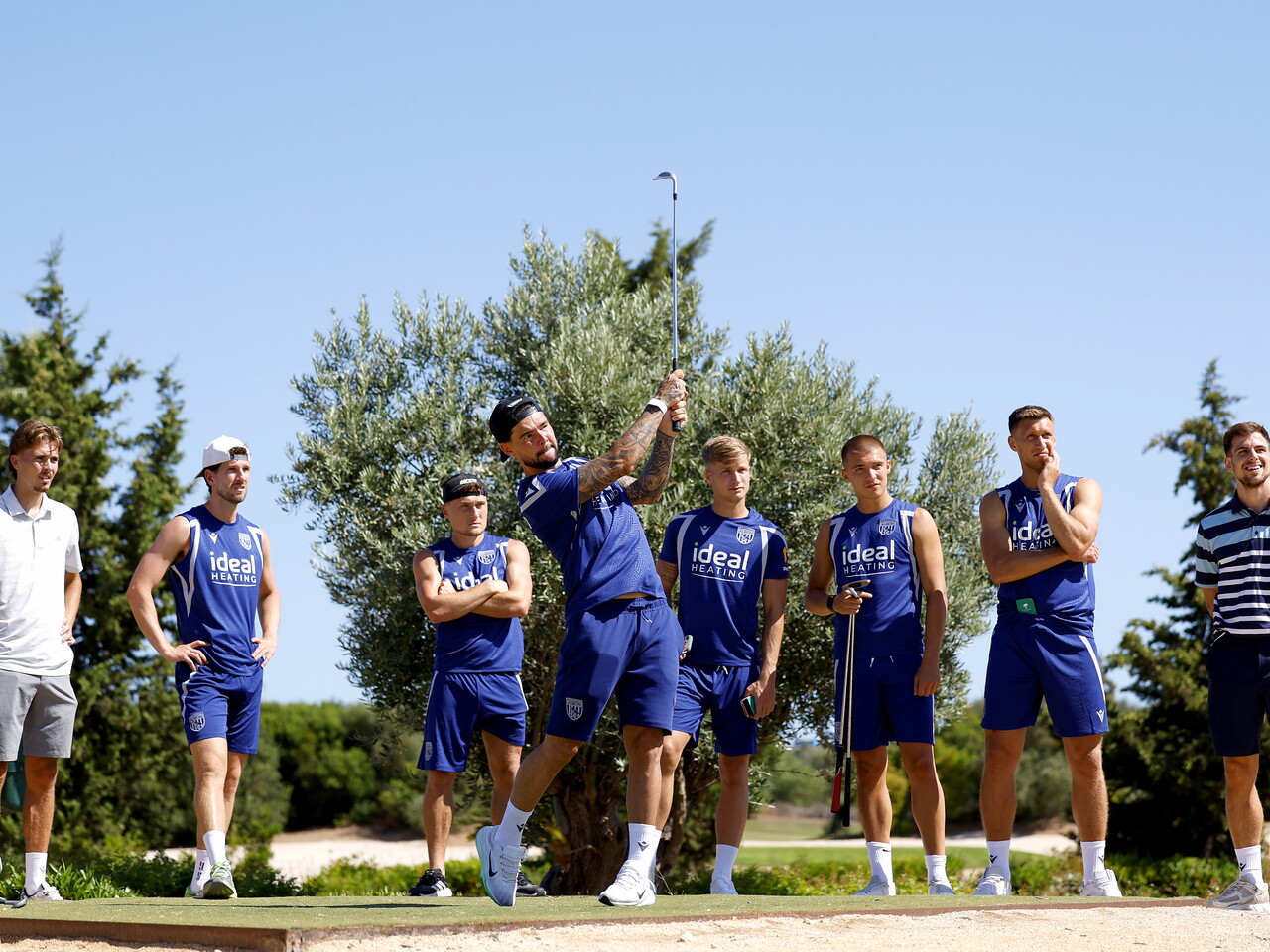 Alex Mowatt hitting a golf shot with several team-mates watching 