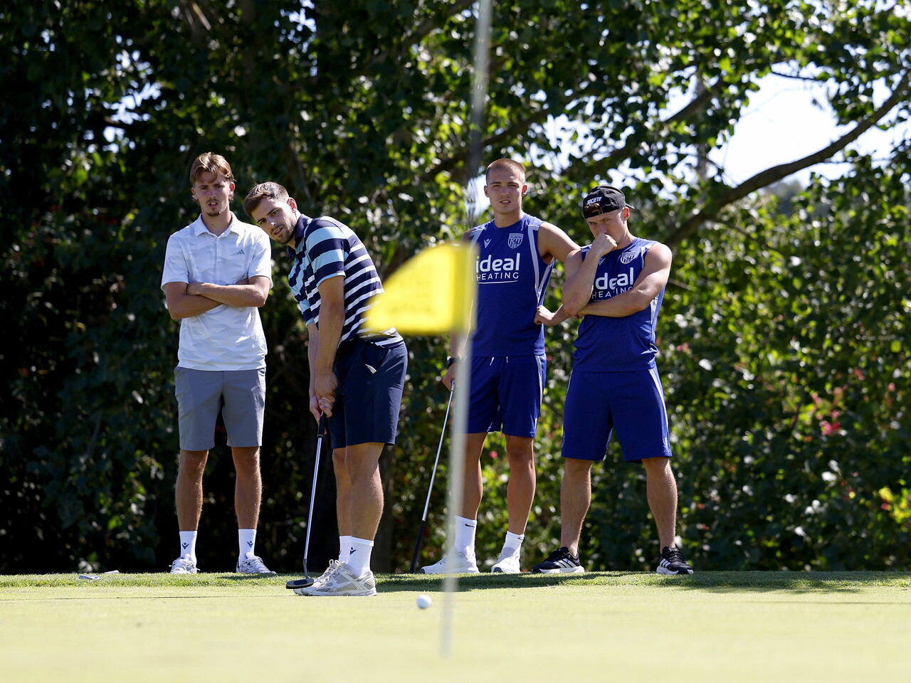 Jayson Molumby putting a golf ball on a green with several WBA team-mates watching 