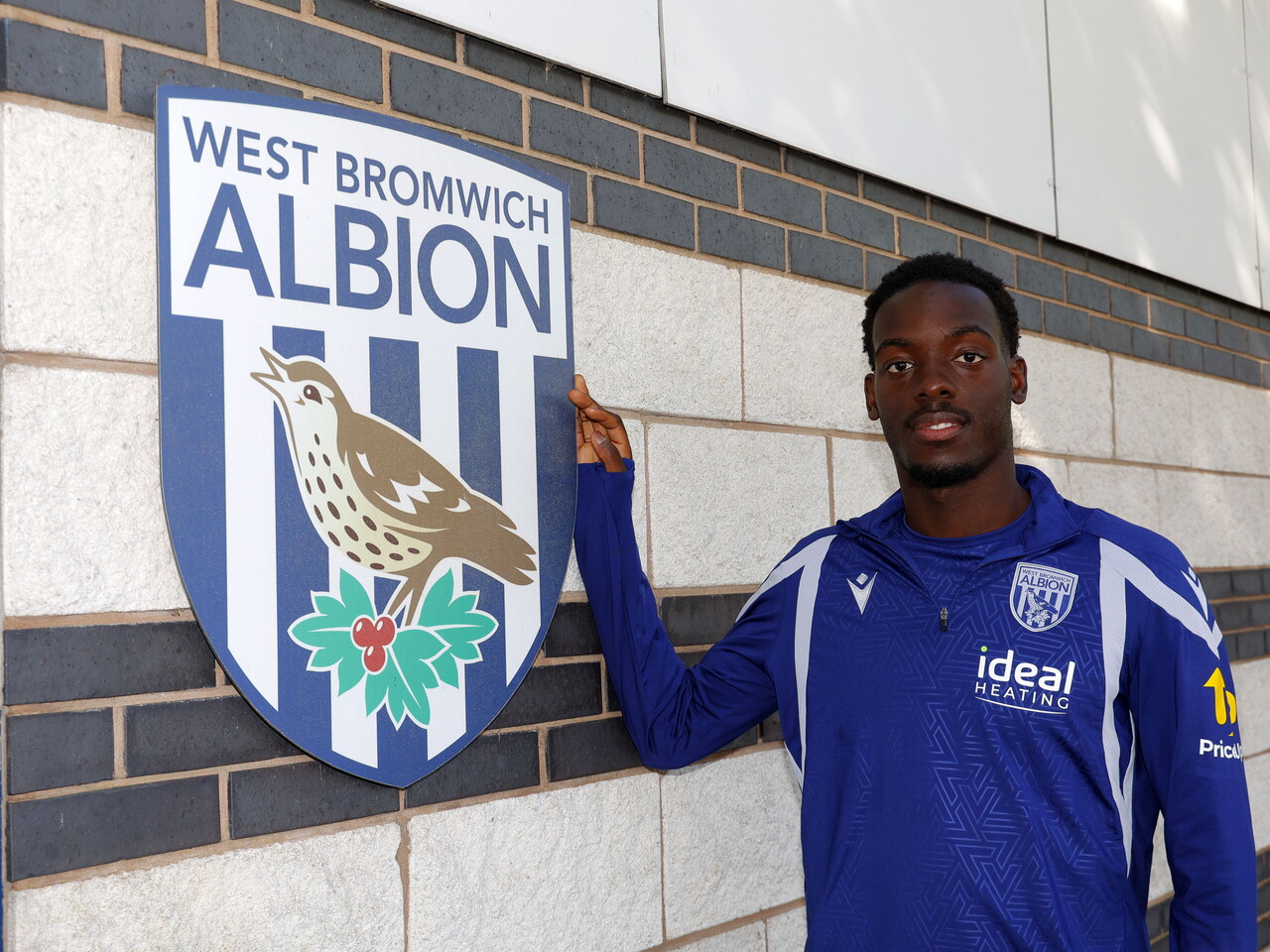 Rabby Nzingoula poses next to a club crest at the training ground