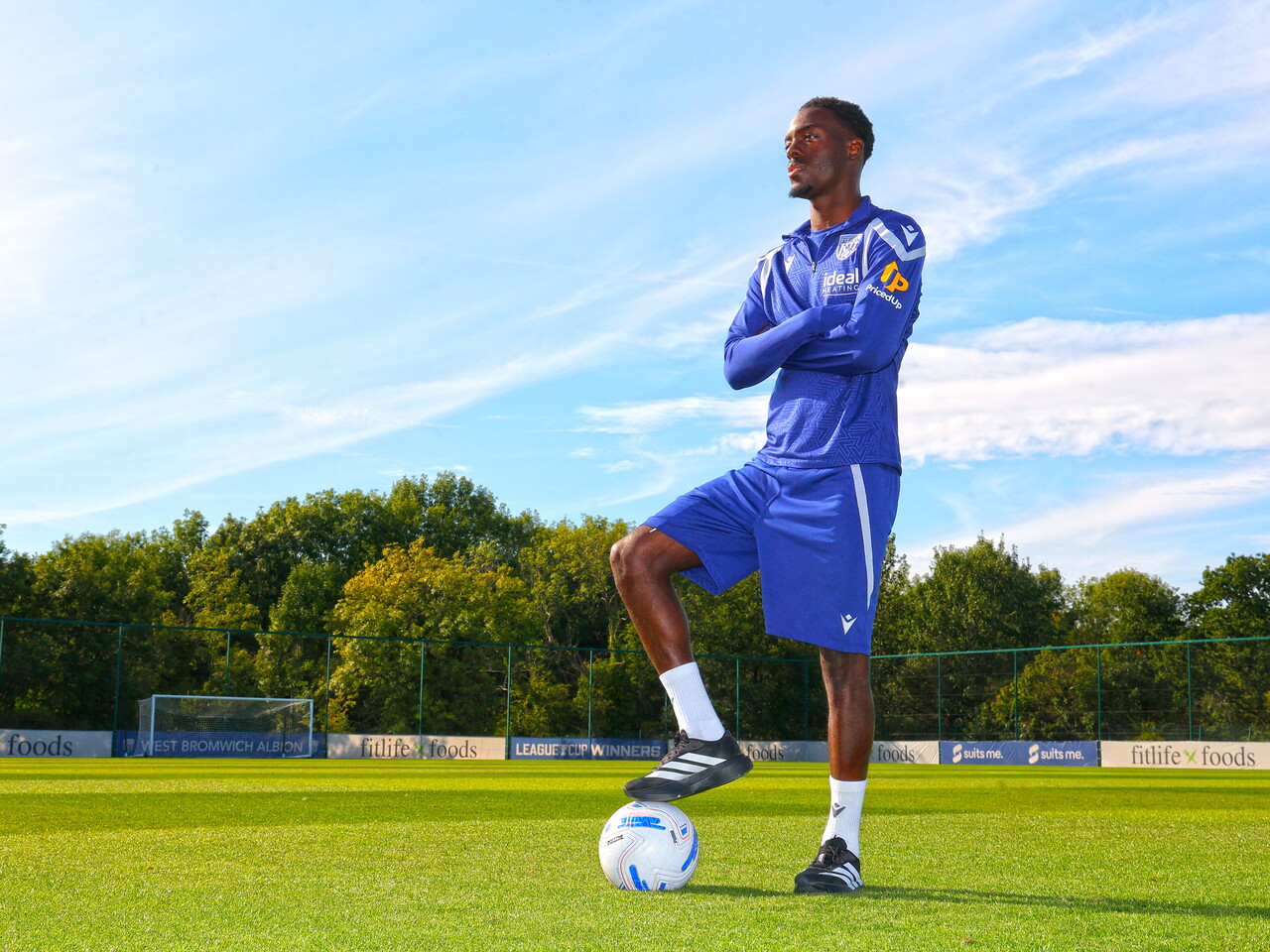 Rabby Nzingoula poses on the training pitch with his arms folded and his foot on a football