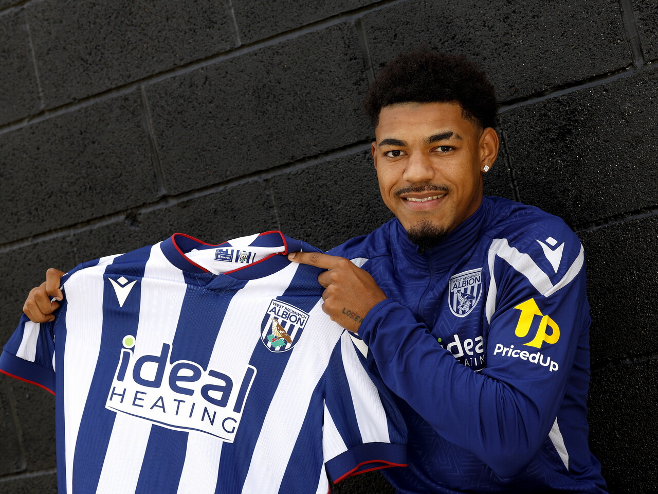 Kareem Tunde smiling at the camera while holding up a home WBA shirt