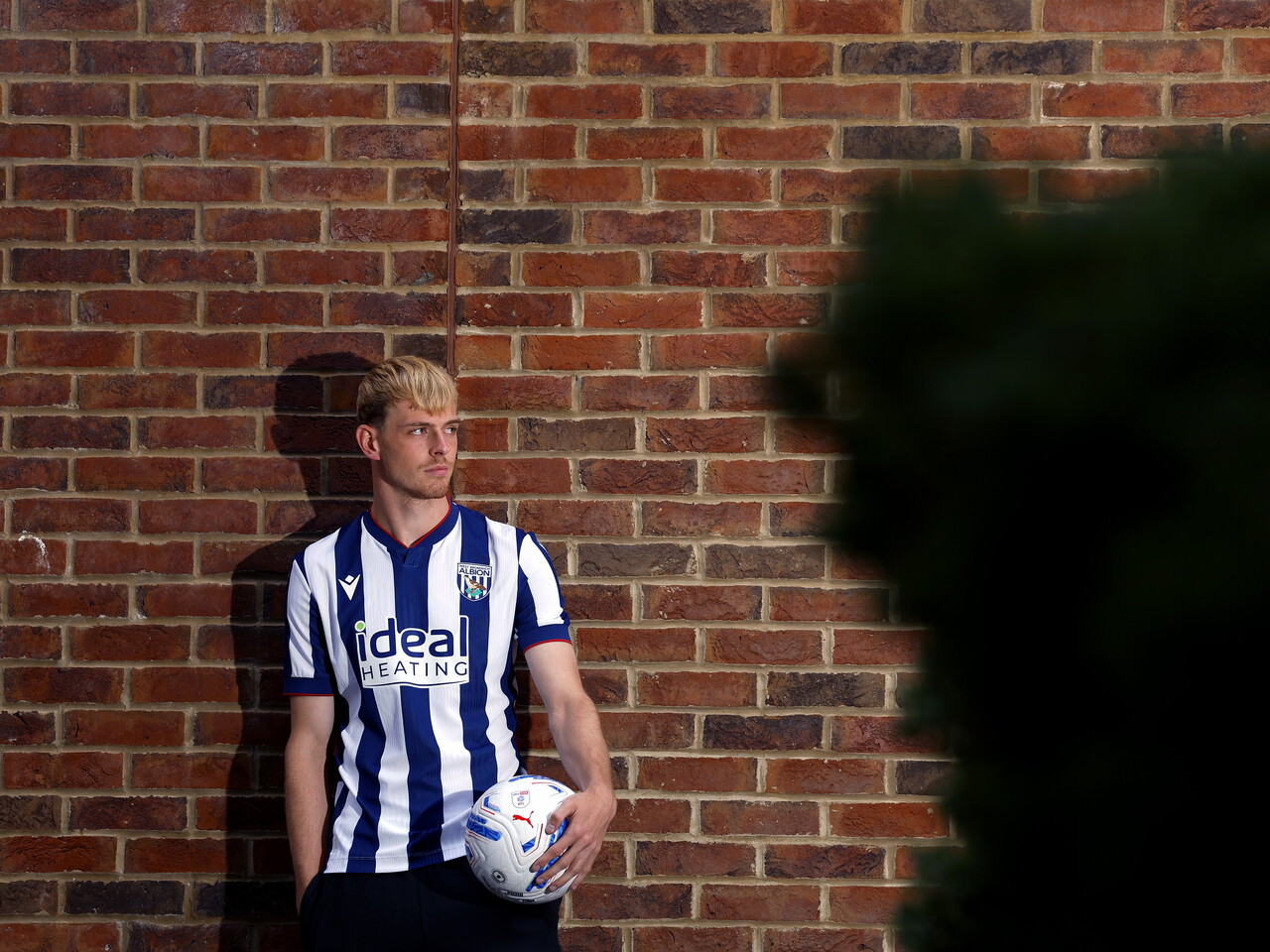 Toby Collyer poses against a brick wall with a ball in his left hand