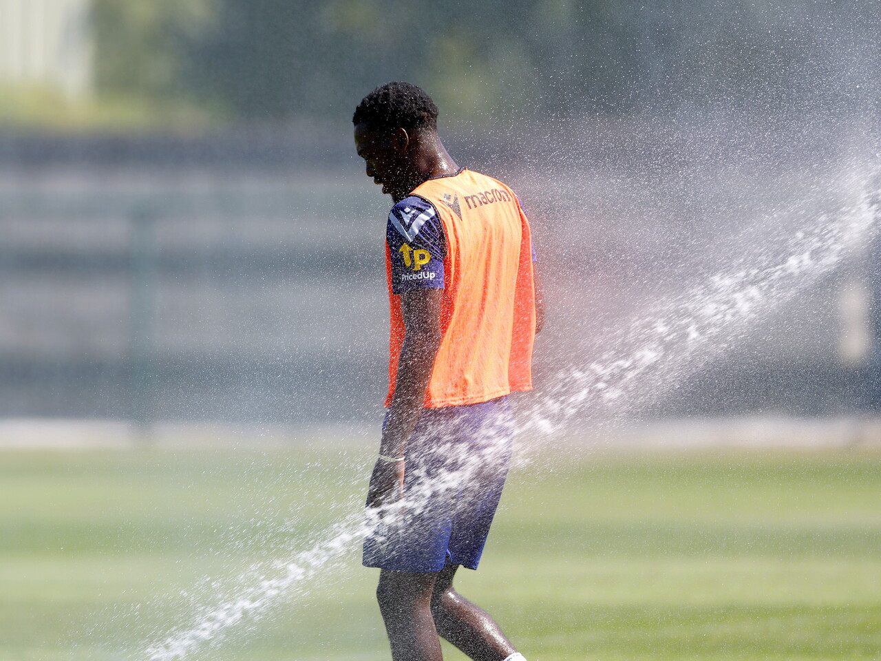 Rabby Nzingoula facing away from camera during a training session with a sprinkler spraying water 