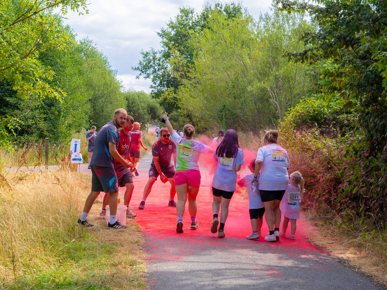 Participants walk through a cloud of pink color powder on a path.