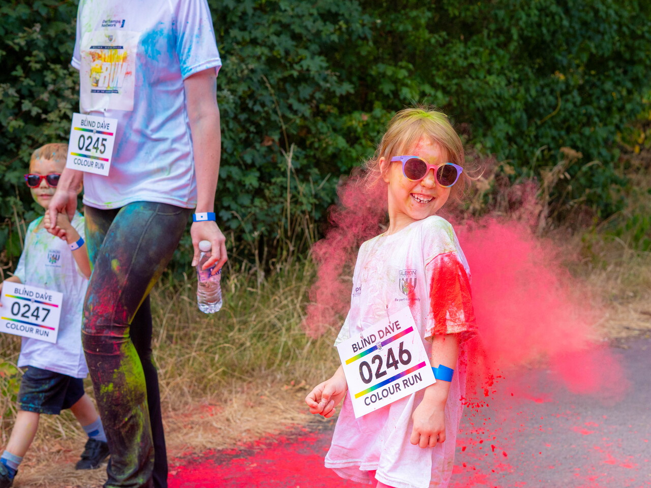 A child participant walks beside an adult while covered in pink powder.