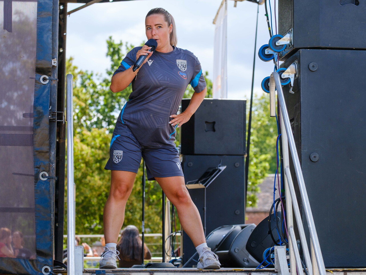 Albion Foundation staff member leads a warm-up from the event stage using a microphone before the charity colour run.
