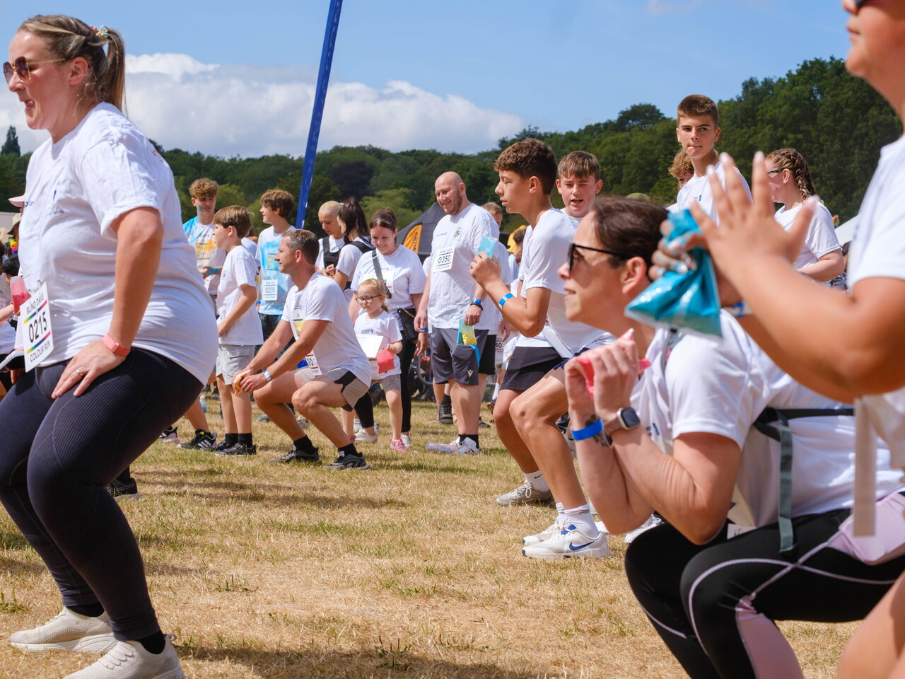 Colour run participants follow a group warm-up activity on an open field, performing exercises before the event begins.