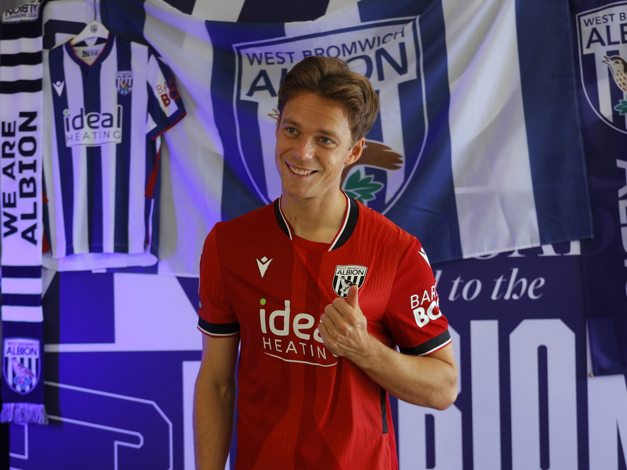 Felix Horn Myhre celebrating towards the camera in the red away kit in front of WBA branding
