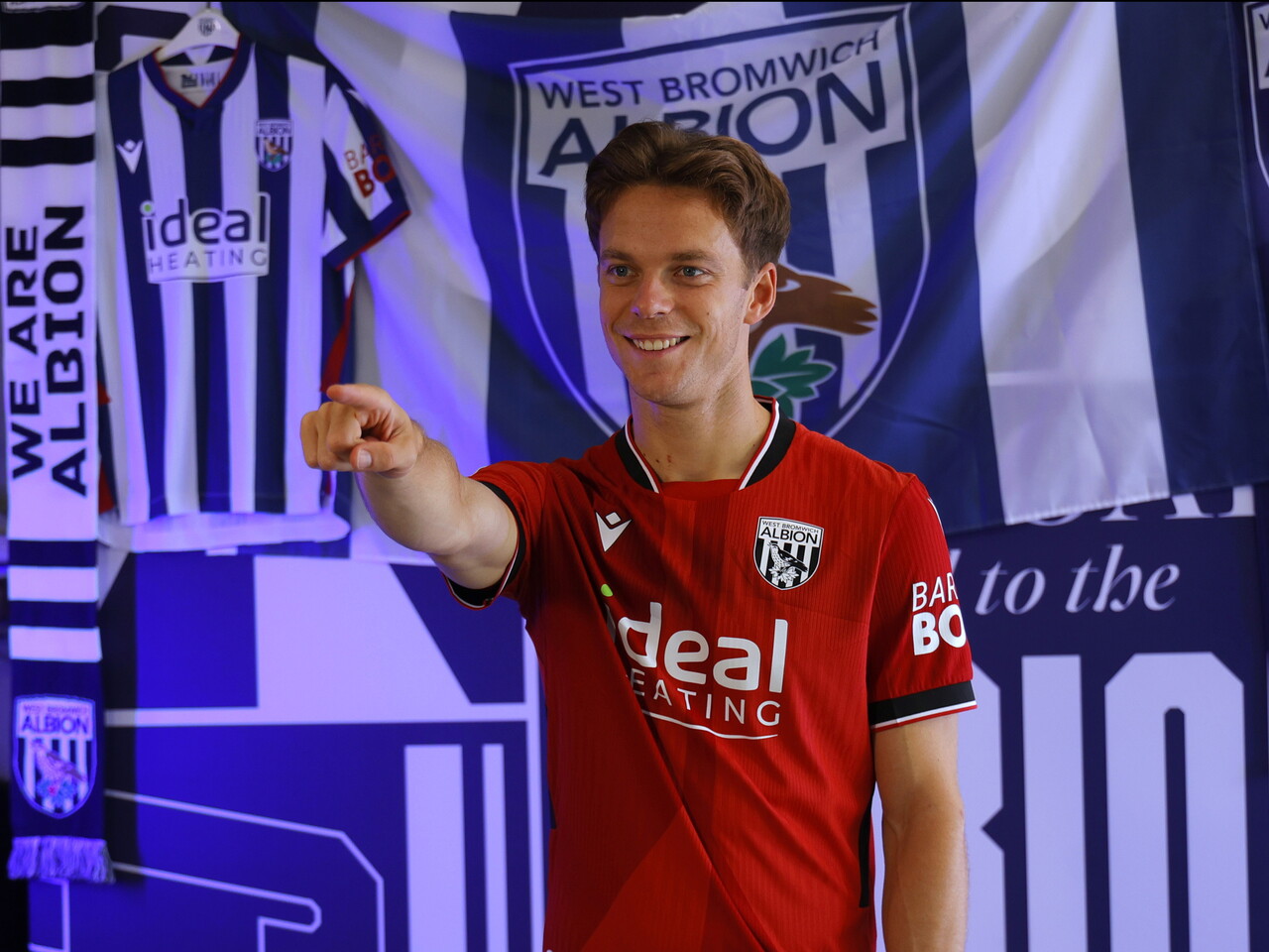 Felix Horn Myhre pointing towards the camera in the red away kit in front of WBA branding