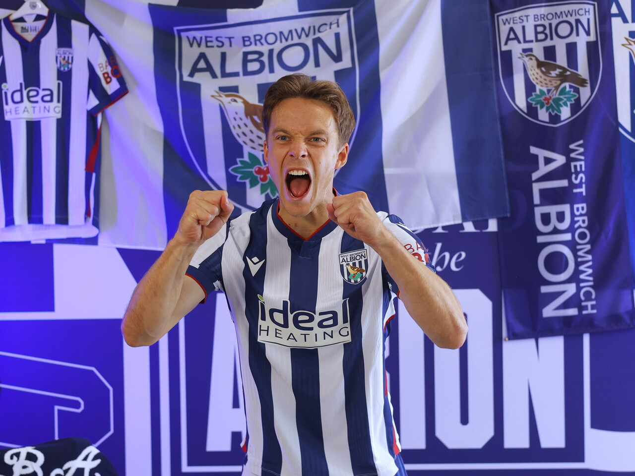 Felix Horn Myhre celebrating towards the camera while sat in the home kit in front of WBA branding