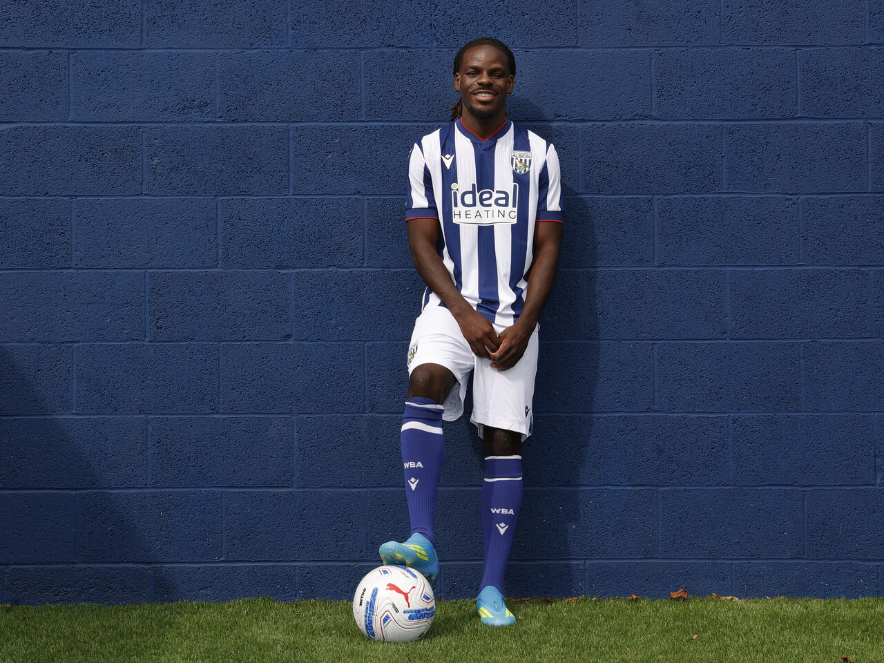 Brayann Pereira smiling at the camera while stood up against a blue wall in the home kit