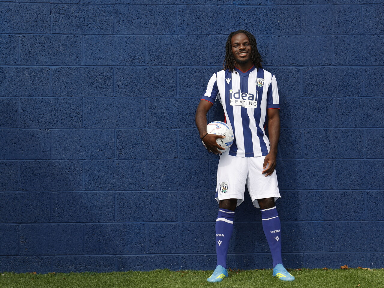 Brayann Pereira smiling at the camera while stood up against a blue wall in the home kit