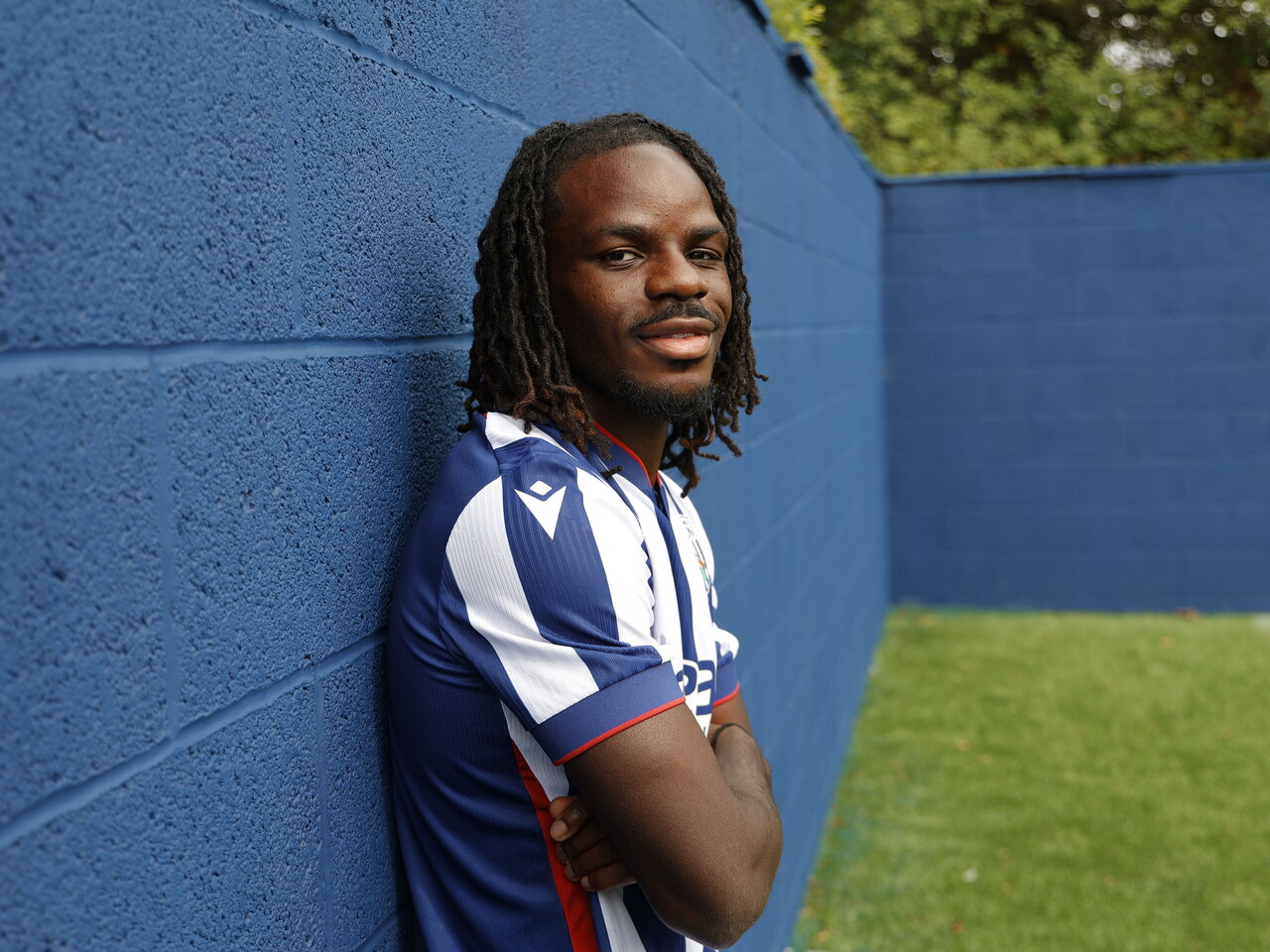 Brayann Pereira smiling at the camera while stood up against a blue wall in the home kit