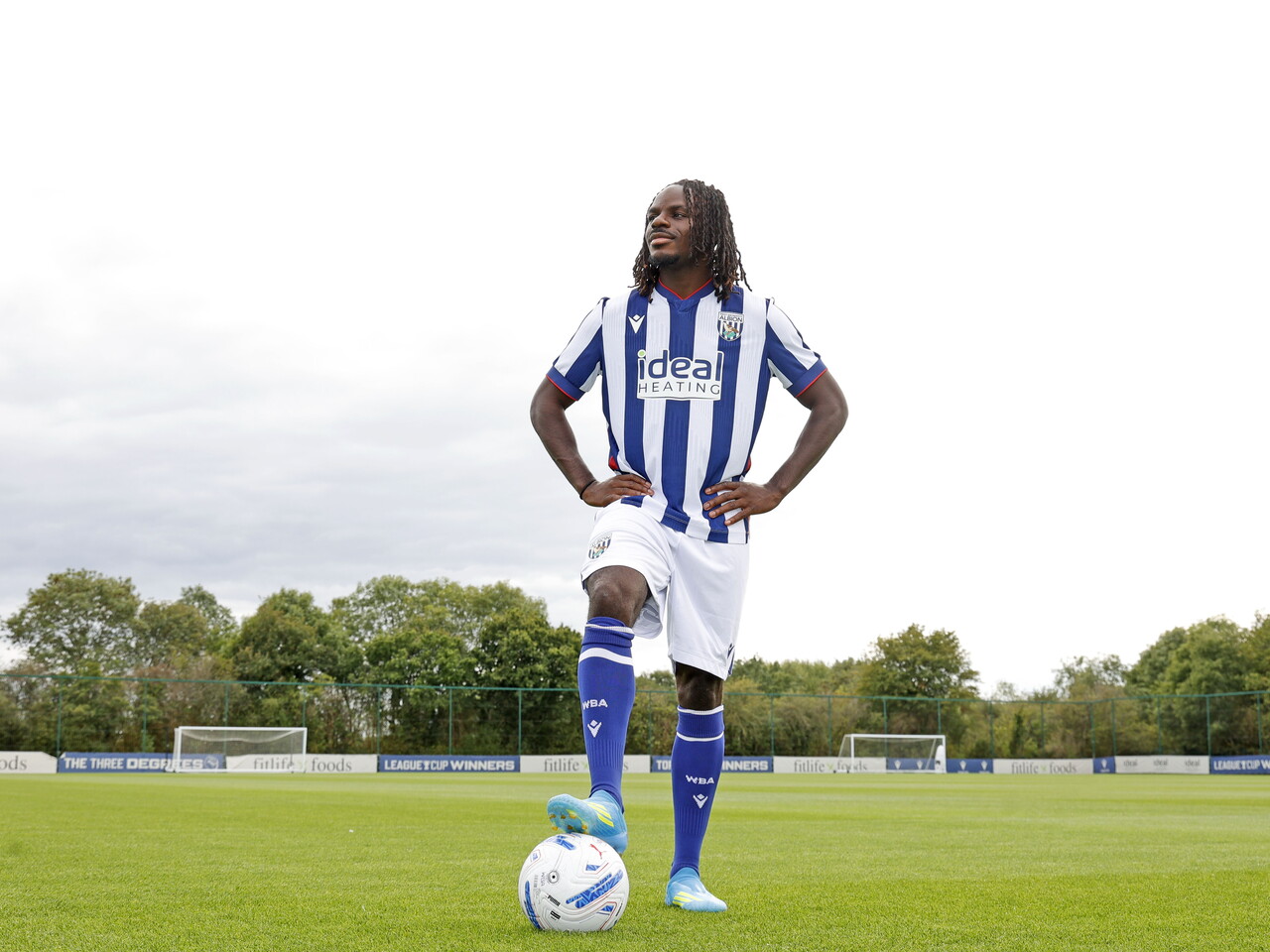 Brayann Pereira smiling at the camera while stood in the home kit with his foot on a ball on a training pitch