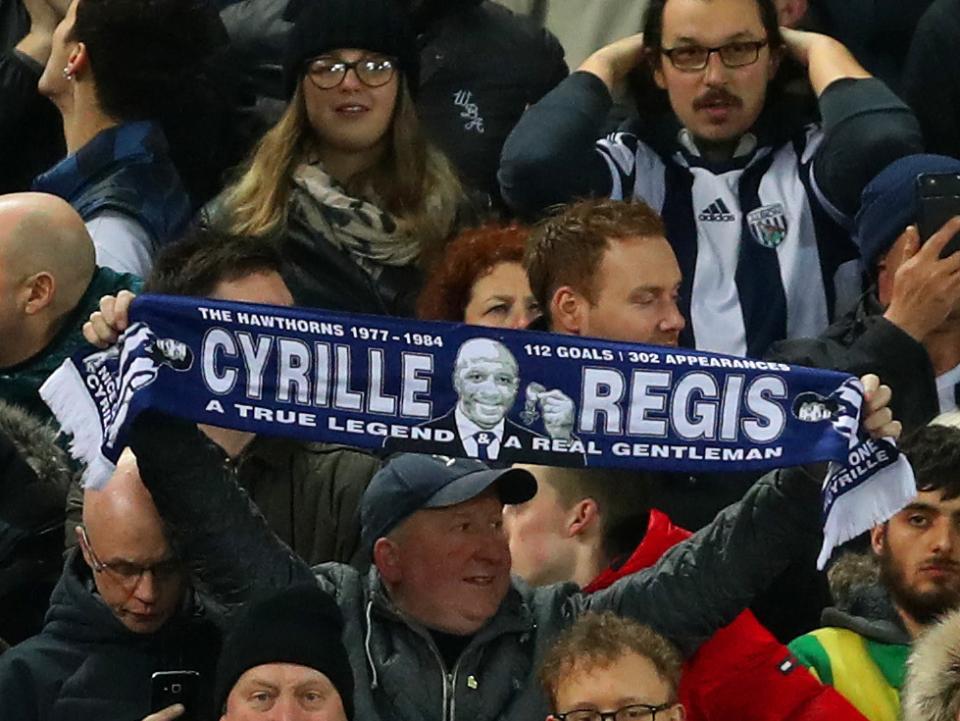 An Albion fan holds up a scarf with Cyrille Regis' name on 