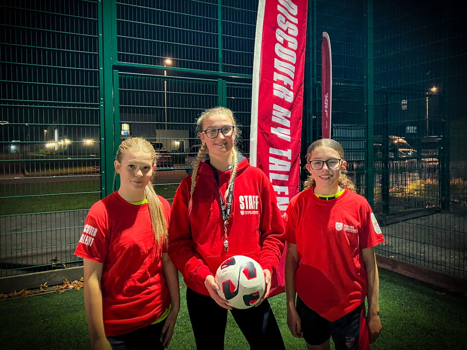 Three girls standing toward with girl in the middle holding a football