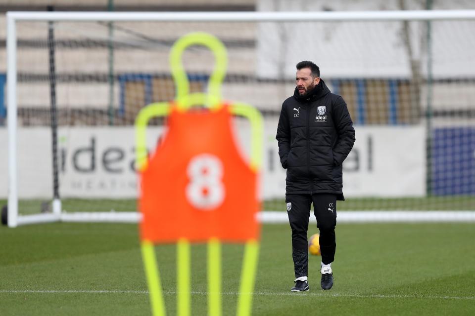 Carlos Corberán standing in the distance on the training pitch with a mannequin in front of him