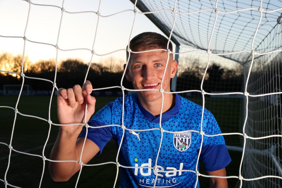 Callum Marshall smiling at the camera while holding onto a goal net