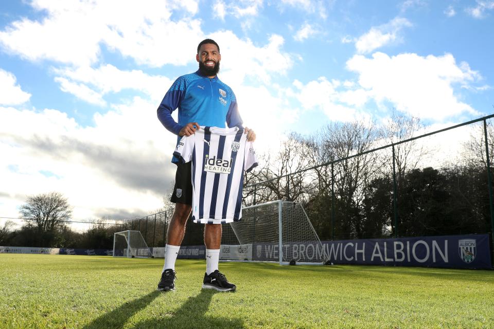 Yann M'Vila posing for a photo stood on the training pitch while holding a home shirt