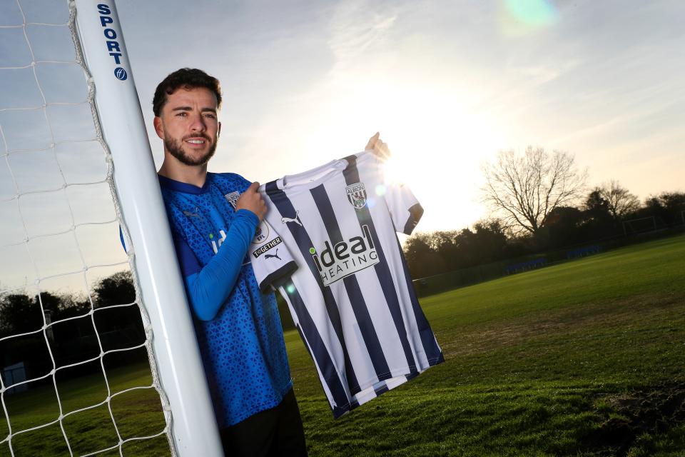 Mikey Johnston smiling at the camera holding up a home Albion shirt