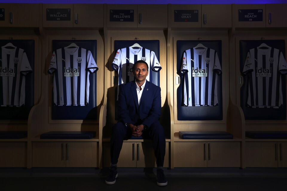 Shilen Patel sitting in the home dressing room looking at the camera surrounded by WBA home shirts