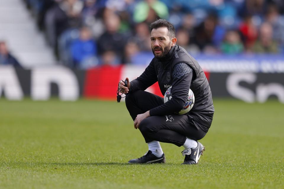Carlos Corberán crouching down holding a football during a training session at The Hawthorns