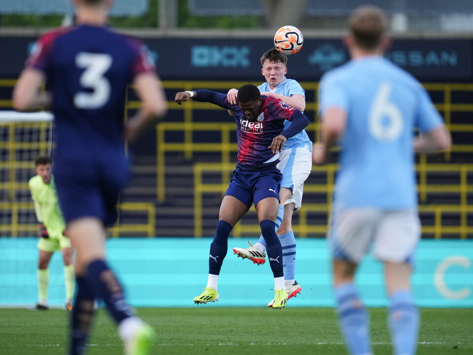 A photo of Josh Maja, in the 23/24 red and blue away kit, jumping for a header in a PL2 game v Man City