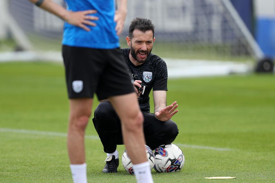 Carlos Corberán crouched down on the training pitch by a ball 