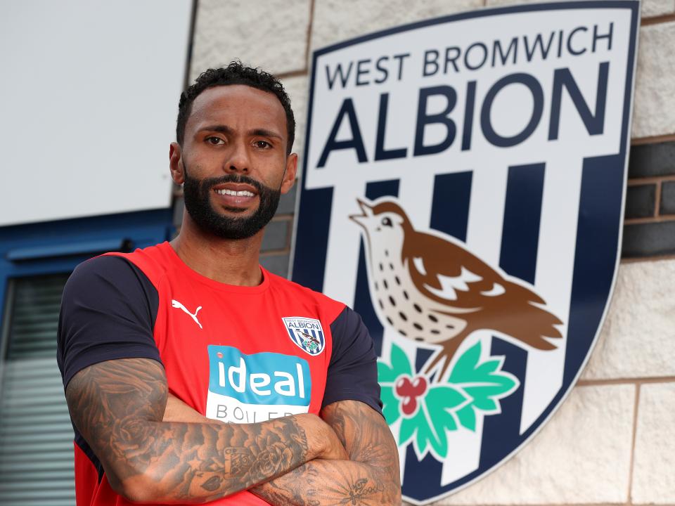 Kyle Bartley posing for a photo in front of the Albion badge with his arms folded 