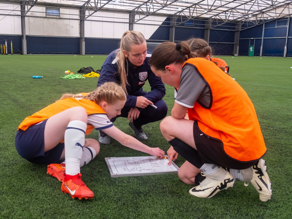A group of girls camp participants take instructions from a camp leader whilst grouped in a huddle.