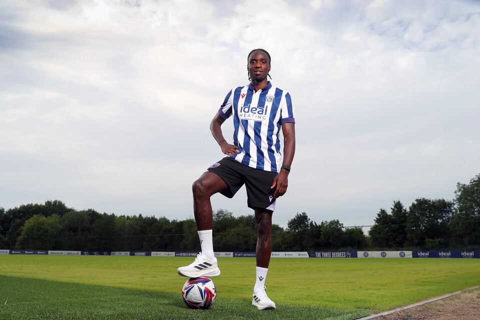 Devante Cole standing with his foot on a ball while smiling at the camera and wearing the home shirt 