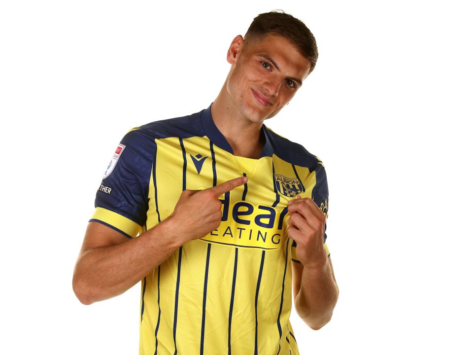 Caleb Taylor pointing to the badge on the yellow away shirt 
