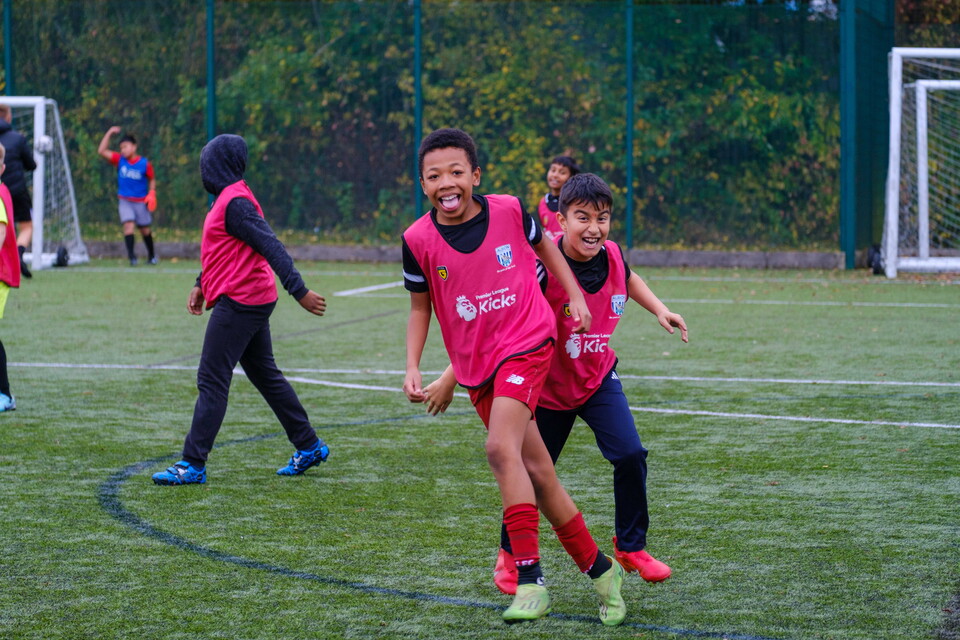 Two players celebrating in pink Premier League Kicks bibs.