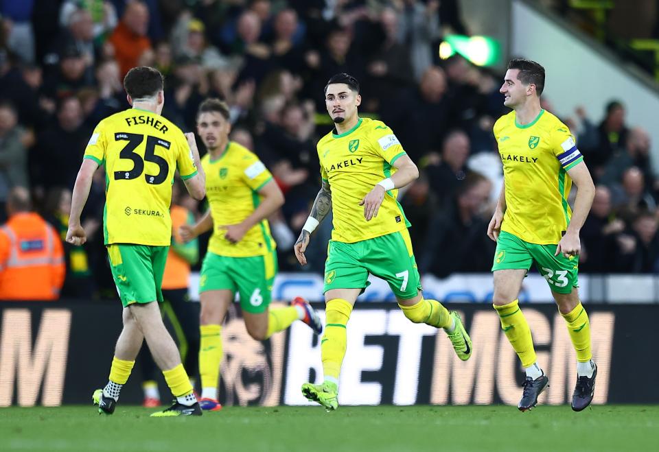 Four Norwich City players in their home kit celebrate a goal